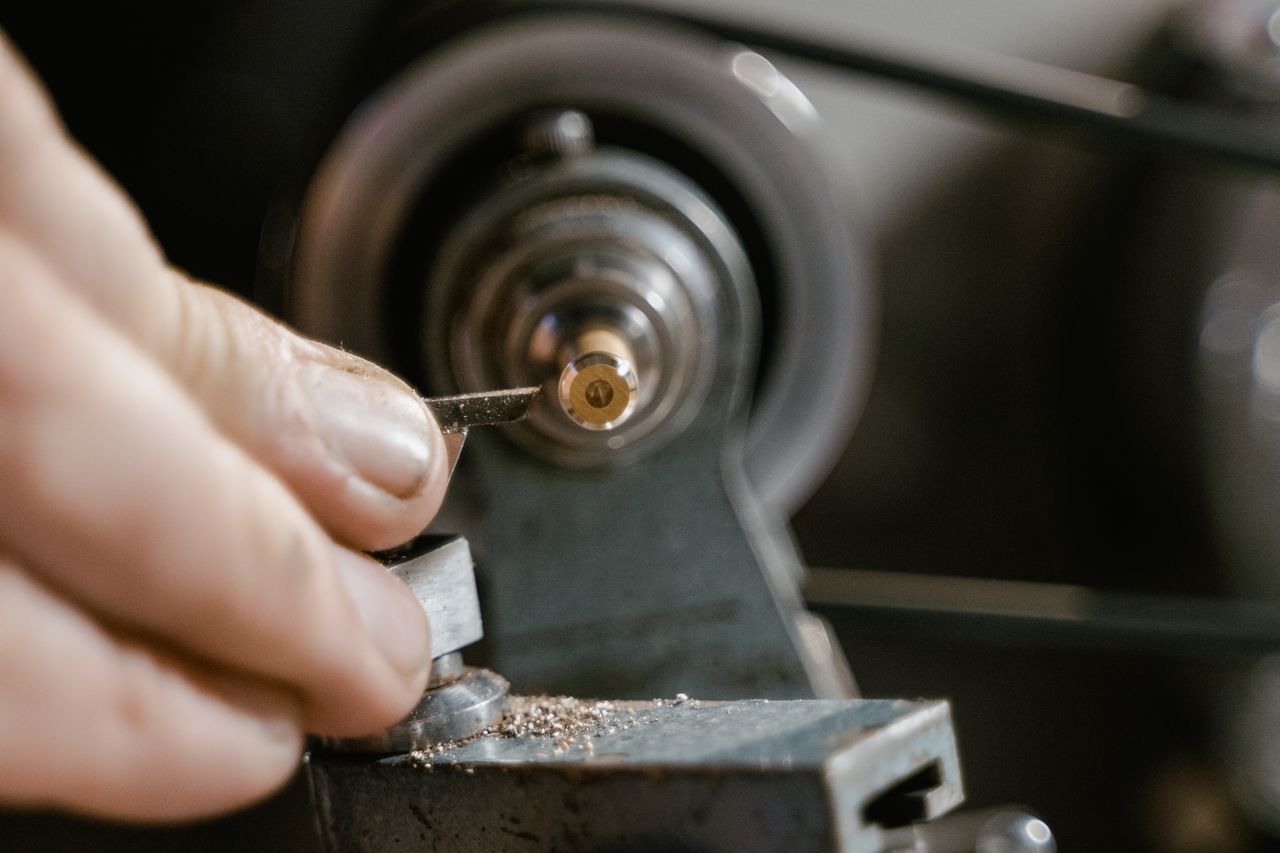 faq-img Detailed view of hands crafting a metal component on a lathe. Precision and skill in focus.
